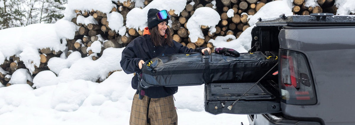 snowboarder putting the bataleon snowboard bag in the bag of the car trunk to safely travel with her snowboard gear