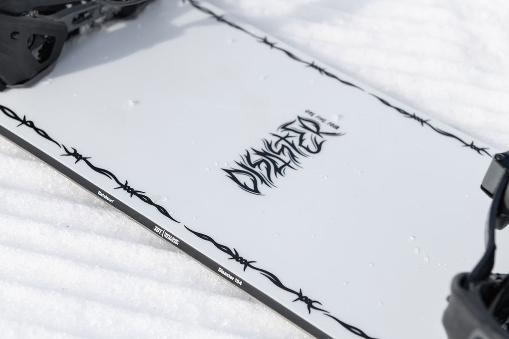 Disaster snowboard laying in the snow focussed on the center graphic